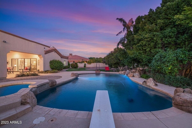 pool at dusk with a diving board, a patio area, and pool water feature