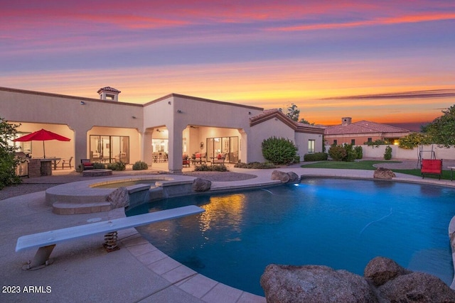 pool at dusk featuring an in ground hot tub, a diving board, and a patio area