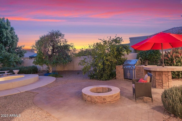 patio terrace at dusk featuring grilling area, exterior kitchen, and a fire pit