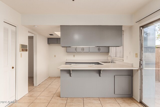 kitchen featuring sink, a kitchen breakfast bar, kitchen peninsula, gray cabinets, and light tile patterned floors