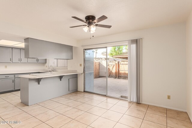 kitchen featuring kitchen peninsula, a kitchen bar, ceiling fan, sink, and light tile patterned floors