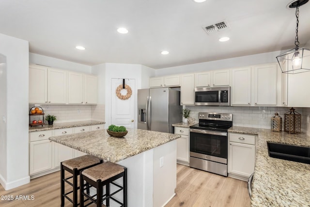 kitchen with light stone countertops, decorative light fixtures, a kitchen island, white cabinetry, and stainless steel appliances