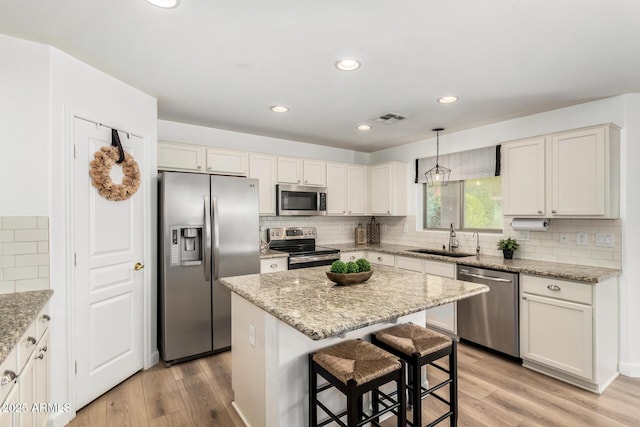 kitchen with sink, hanging light fixtures, stainless steel appliances, light stone counters, and a kitchen island