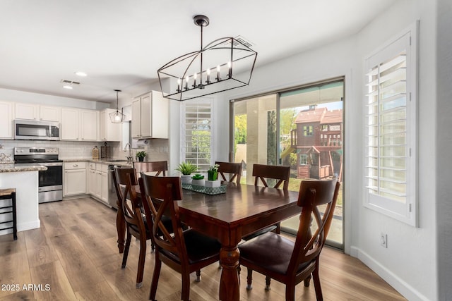 dining area with sink, light hardwood / wood-style floors, and a notable chandelier