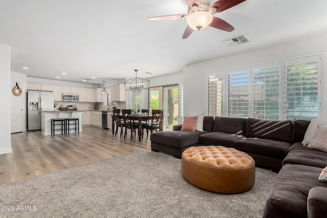 living room with light hardwood / wood-style flooring and ceiling fan with notable chandelier