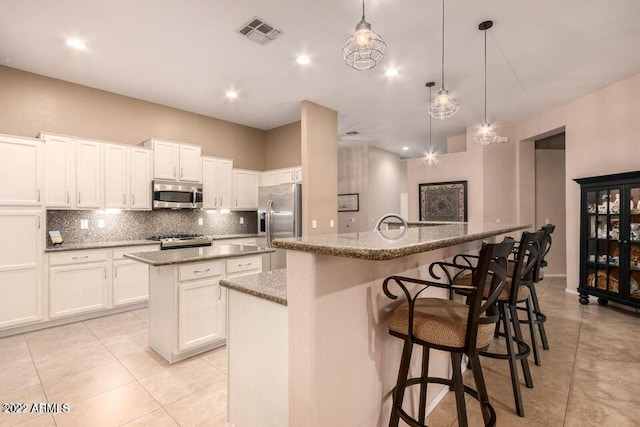 kitchen featuring a kitchen island with sink, hanging light fixtures, white cabinetry, and stainless steel appliances