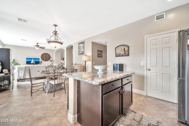 kitchen featuring pendant lighting, a center island, light tile patterned floors, light stone countertops, and dark brown cabinets