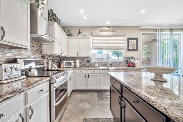 kitchen featuring sink, light stone counters, double oven range, wall chimney range hood, and white cabinets