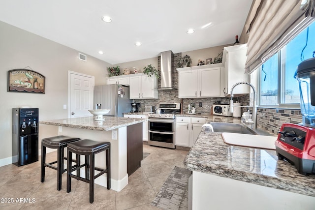 kitchen featuring wall chimney exhaust hood, white cabinetry, appliances with stainless steel finishes, a kitchen island, and backsplash