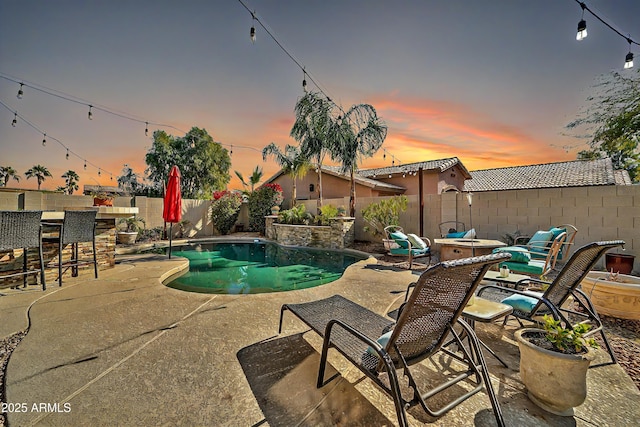 pool at dusk featuring a bar and a patio