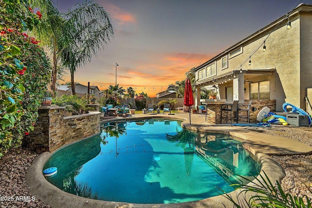 pool at dusk with a patio area and an outdoor bar