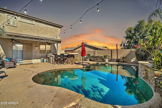 pool at dusk with exterior bar, ceiling fan, and a patio area