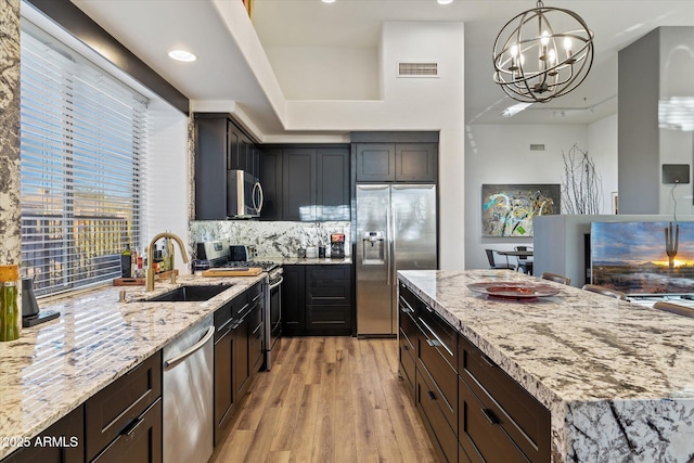 kitchen featuring hanging light fixtures, light stone counters, a notable chandelier, decorative backsplash, and appliances with stainless steel finishes