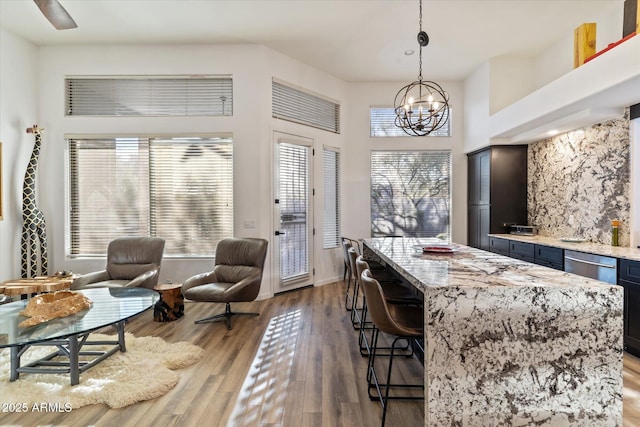 bar with an inviting chandelier, hanging light fixtures, light stone countertops, a towering ceiling, and light hardwood / wood-style floors