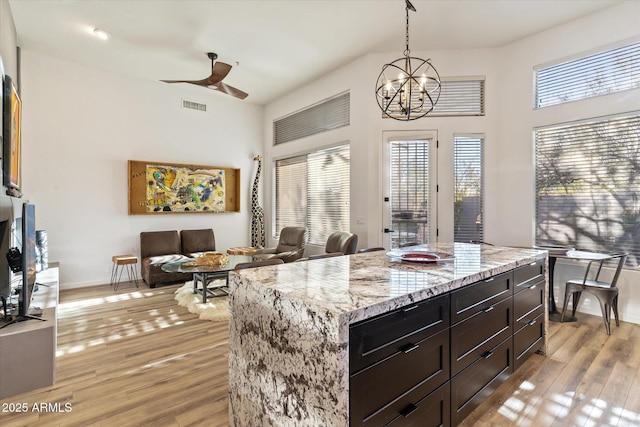 kitchen featuring light stone countertops, ceiling fan with notable chandelier, pendant lighting, light hardwood / wood-style flooring, and a kitchen island