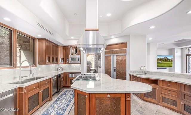 kitchen featuring brown cabinets, a kitchen island, a sink, light stone countertops, and built in appliances