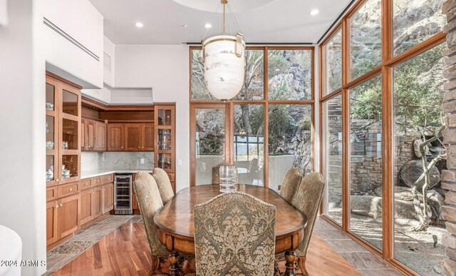 dining space featuring light hardwood / wood-style flooring, expansive windows, a high ceiling, and beverage cooler