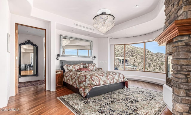 bedroom featuring a chandelier, a raised ceiling, multiple windows, and wood finished floors