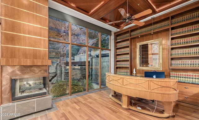 unfurnished office featuring wooden ceiling, wood finished floors, a ceiling fan, built in features, and a multi sided fireplace