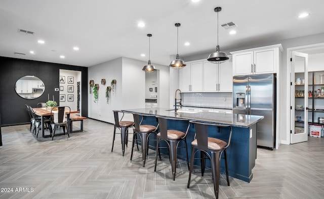 kitchen with light parquet floors, a center island with sink, sink, stainless steel fridge, and stone countertops