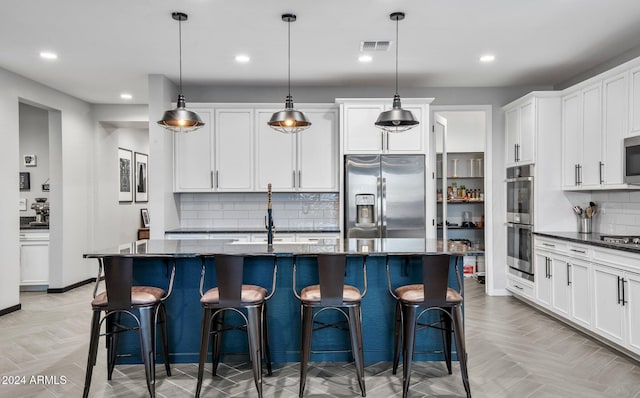 kitchen featuring a kitchen island with sink, light parquet floors, decorative light fixtures, and appliances with stainless steel finishes