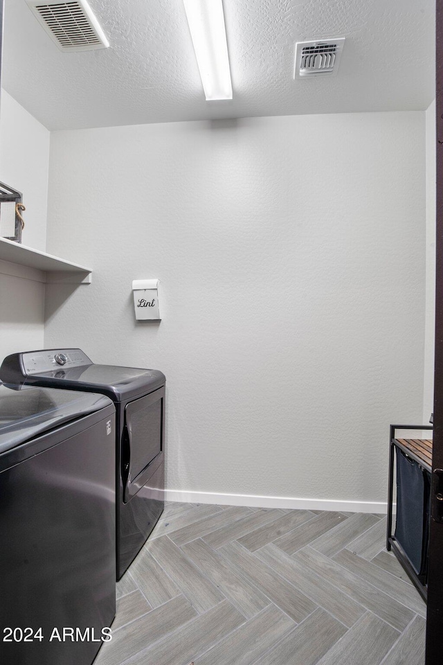 clothes washing area with washing machine and dryer and a textured ceiling