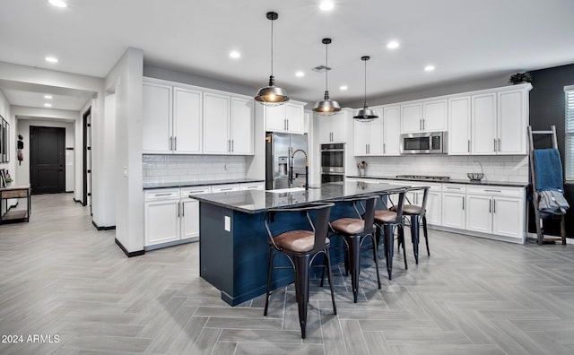 kitchen with decorative light fixtures, a kitchen island with sink, appliances with stainless steel finishes, and light parquet flooring