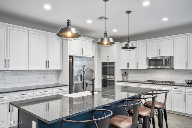 kitchen featuring appliances with stainless steel finishes, dark parquet flooring, a kitchen island with sink, and pendant lighting