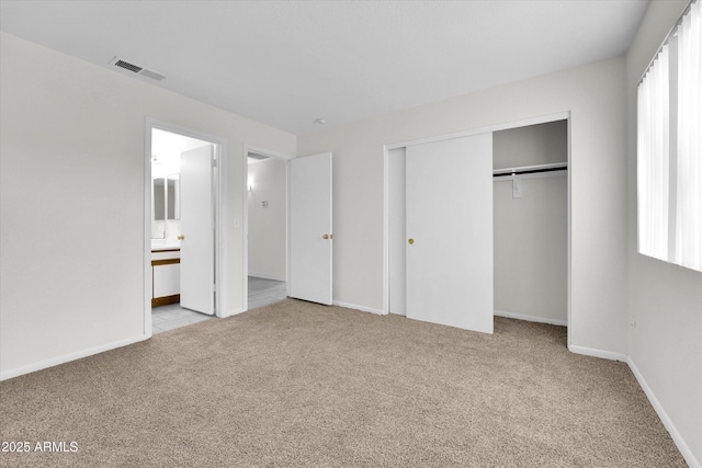 unfurnished bedroom with multiple windows, ensuite bathroom, a closet, and light colored carpet