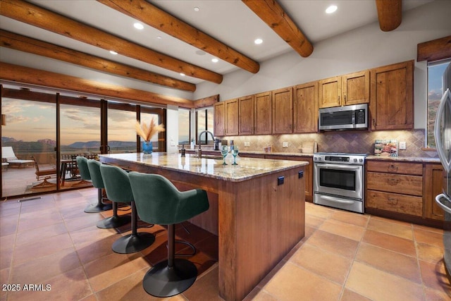 kitchen with light stone countertops, stainless steel appliances, a center island with sink, tasteful backsplash, and sink