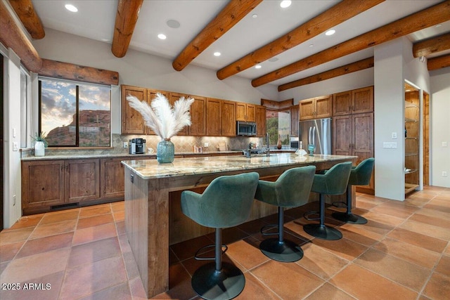 kitchen with light stone counters, a spacious island, tasteful backsplash, appliances with stainless steel finishes, and a kitchen breakfast bar