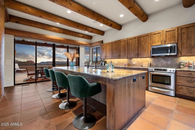 kitchen with stainless steel appliances, sink, backsplash, and an island with sink