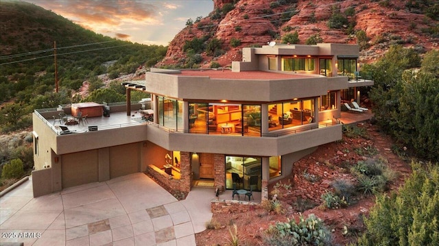 back house at dusk with a balcony, a patio, and an outdoor fireplace