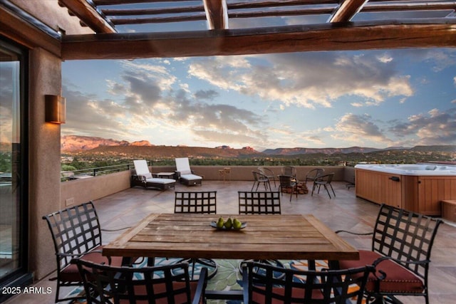 patio terrace at dusk with a hot tub, a pergola, and a mountain view