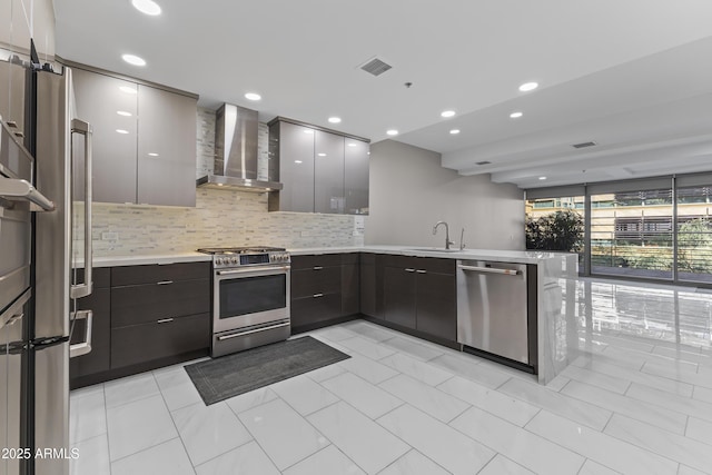 kitchen featuring modern cabinets, a sink, appliances with stainless steel finishes, a peninsula, and wall chimney range hood