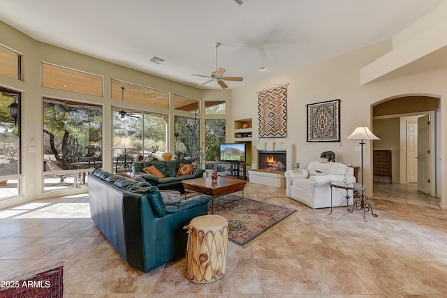 living room with a high ceiling, ceiling fan, a wealth of natural light, and a fireplace