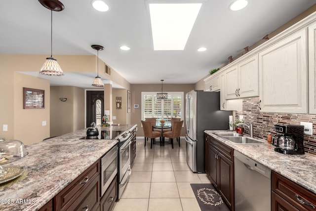 kitchen with a skylight, stainless steel appliances, backsplash, light tile patterned flooring, and a sink