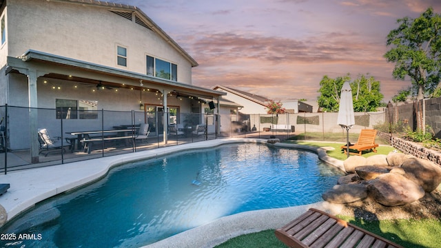 pool at dusk with ceiling fan, fence, and a patio