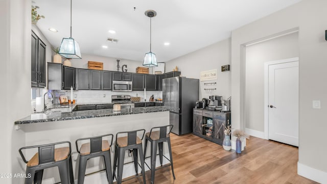 kitchen with stainless steel appliances, a peninsula, dark stone counters, a sink, and backsplash