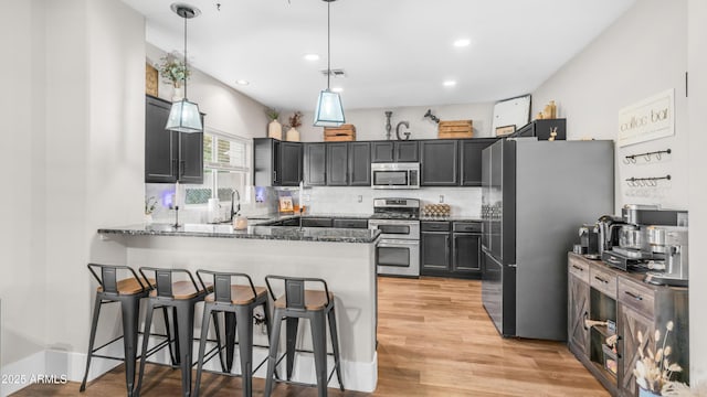 kitchen featuring stainless steel appliances, a peninsula, dark stone countertops, decorative light fixtures, and light wood finished floors