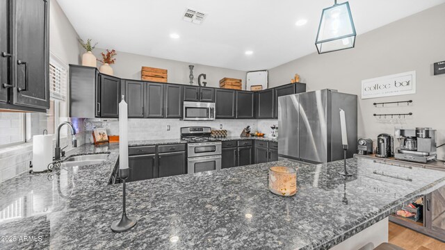kitchen featuring appliances with stainless steel finishes, a peninsula, a sink, dark stone countertops, and recessed lighting