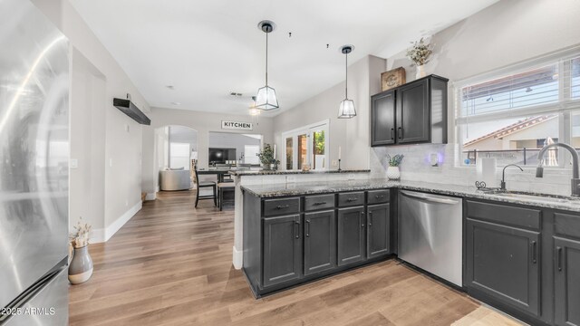 kitchen featuring appliances with stainless steel finishes, a sink, a peninsula, tasteful backsplash, and stone countertops