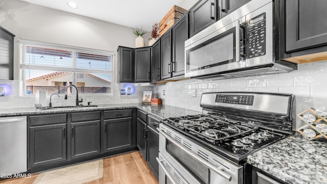kitchen featuring stainless steel appliances, a sink, stone counters, light wood finished floors, and recessed lighting