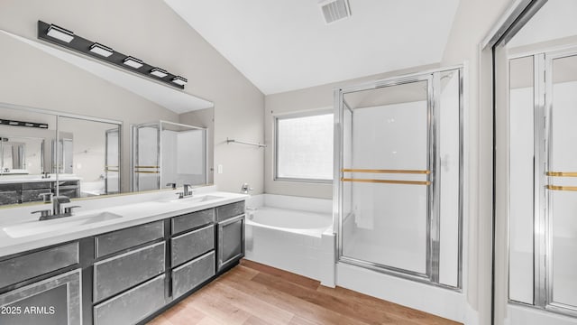 bathroom featuring lofted ceiling, a garden tub, a shower stall, wood finished floors, and double vanity