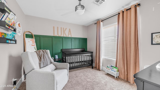 bedroom featuring a crib, light colored carpet, and a ceiling fan