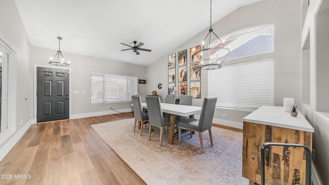 dining room with a chandelier, light wood-style floors, ceiling fan, baseboards, and high vaulted ceiling