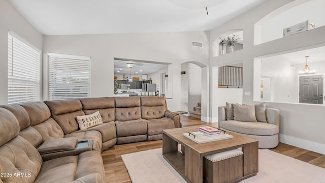 living room featuring light wood finished floors, baseboards, a chandelier, arched walkways, and high vaulted ceiling