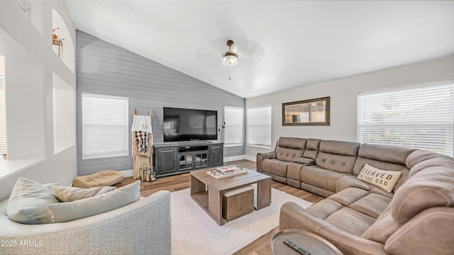 living area with lofted ceiling, light wood-style floors, ceiling fan, wood walls, and baseboards