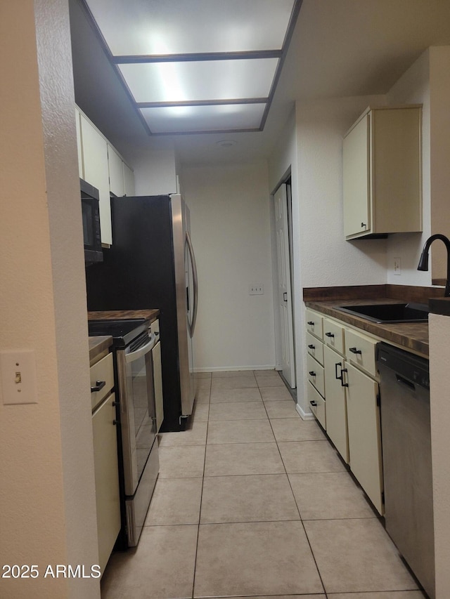 kitchen with stainless steel appliances, dark countertops, a sink, and light tile patterned floors