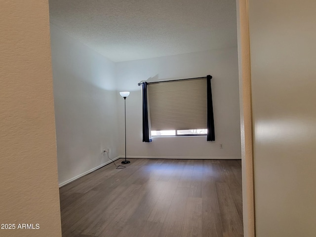 spare room with a textured ceiling, baseboards, and wood finished floors